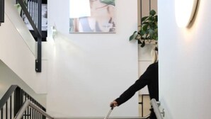 Une personne descend un escalier en tenant une valise rouge.