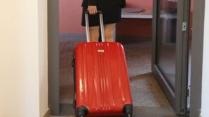 Une personne portant une valise rouge entre dans une pièce dont la porte est en verre.