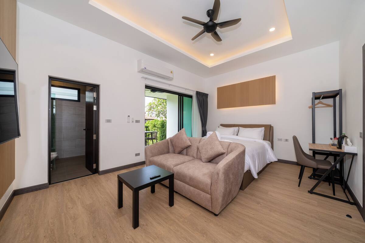 A modern hotel room with a sofa, bed, desk, and ceiling fan.