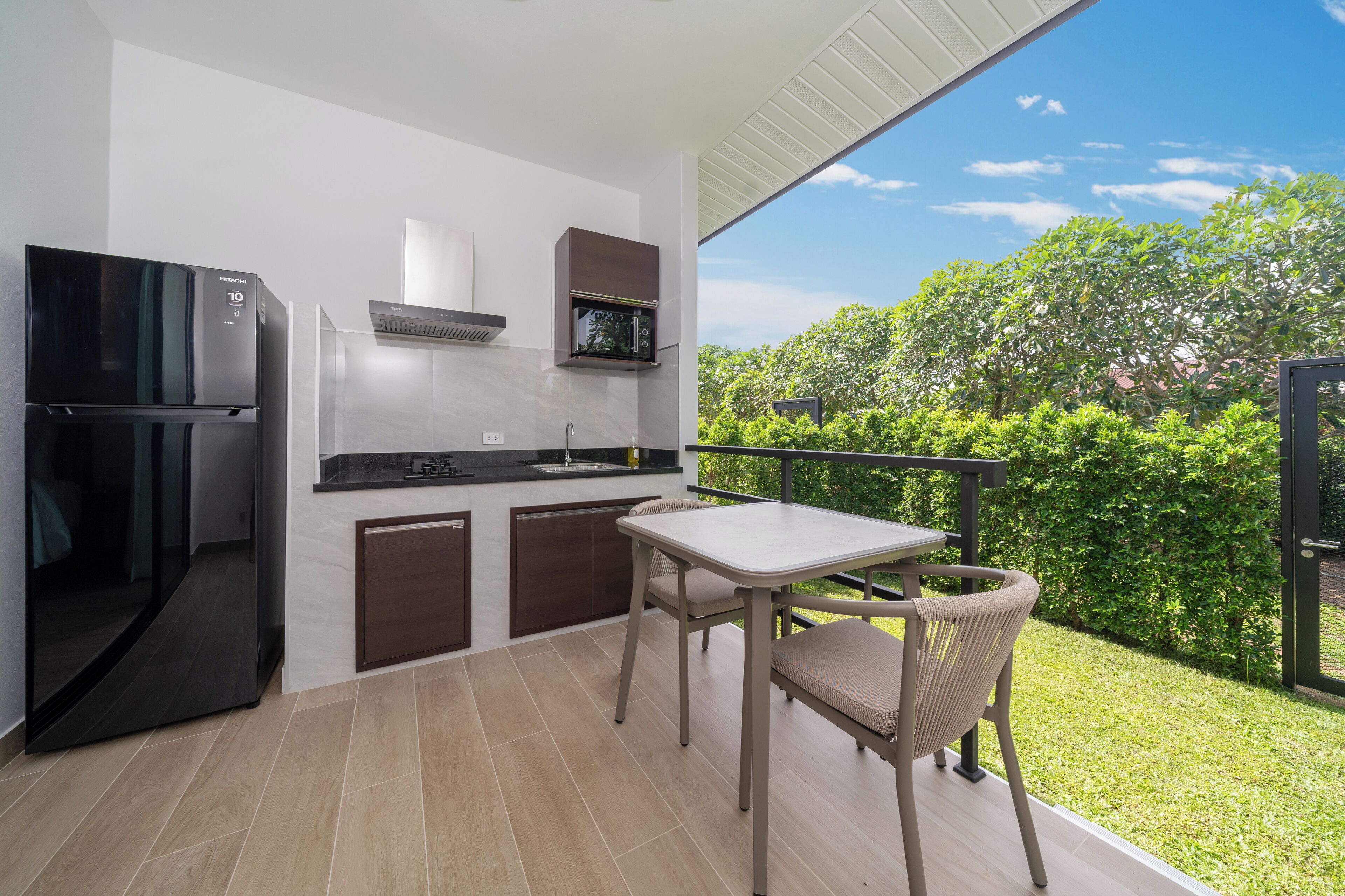 A modern kitchen with a built-in microwave, refrigerator, and stove. There is a dining area with a table and chairs, and a view of a lush garden.