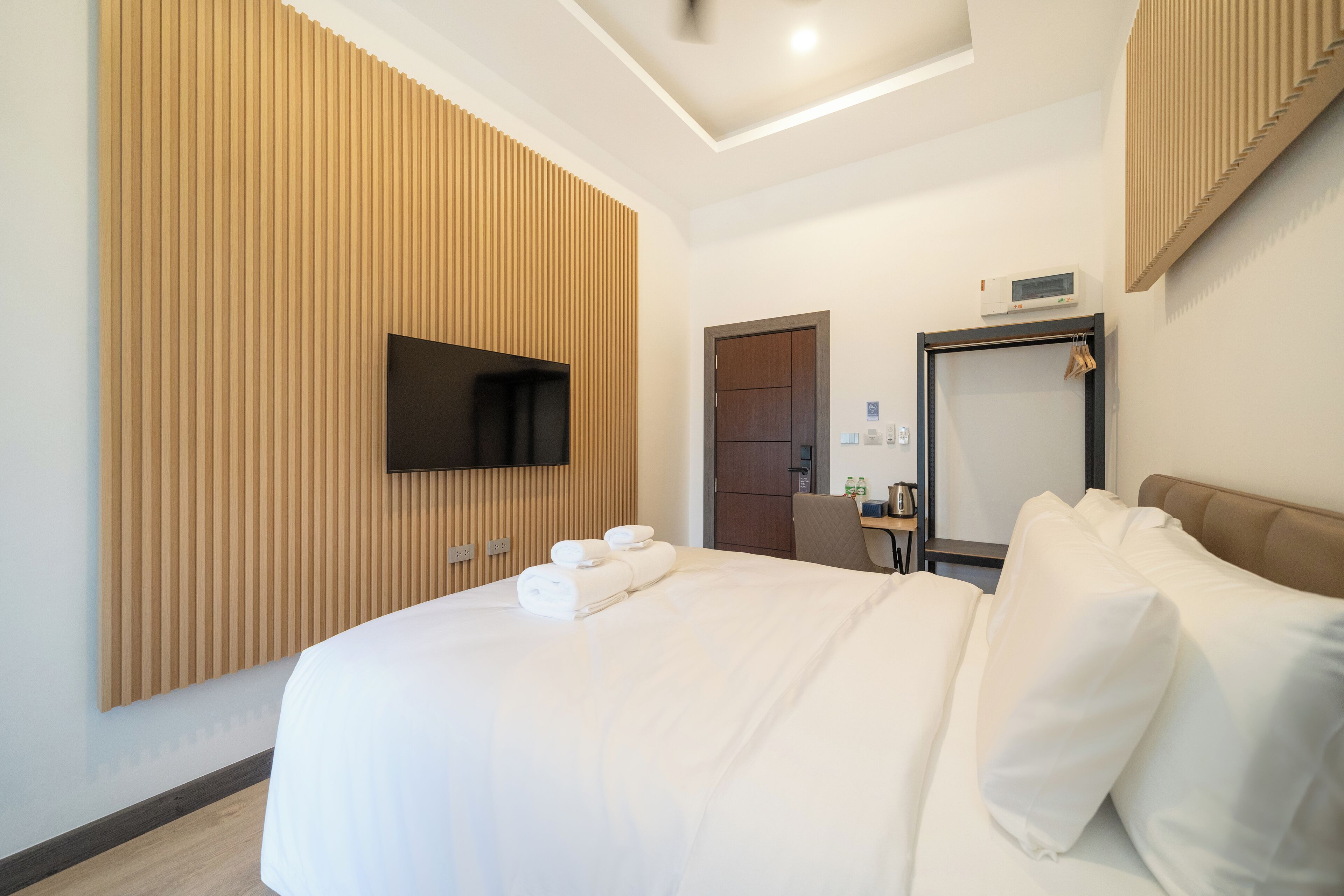 Habitación de hotel con una cama grande, un televisor de pantalla plana montado en la pared, panel de pared de madera, una puerta, un escritorio con silla y un espejo.