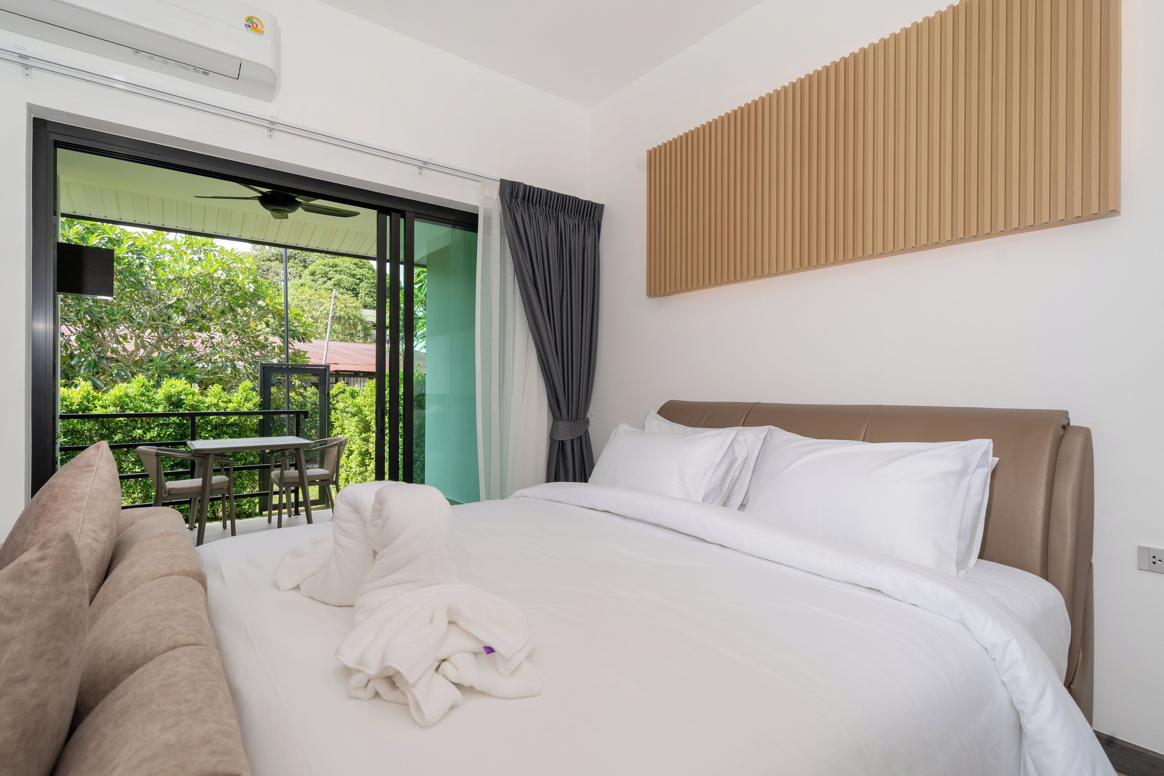 A hotel room with a bed, a sofa, a table, and a view of greenery outside.