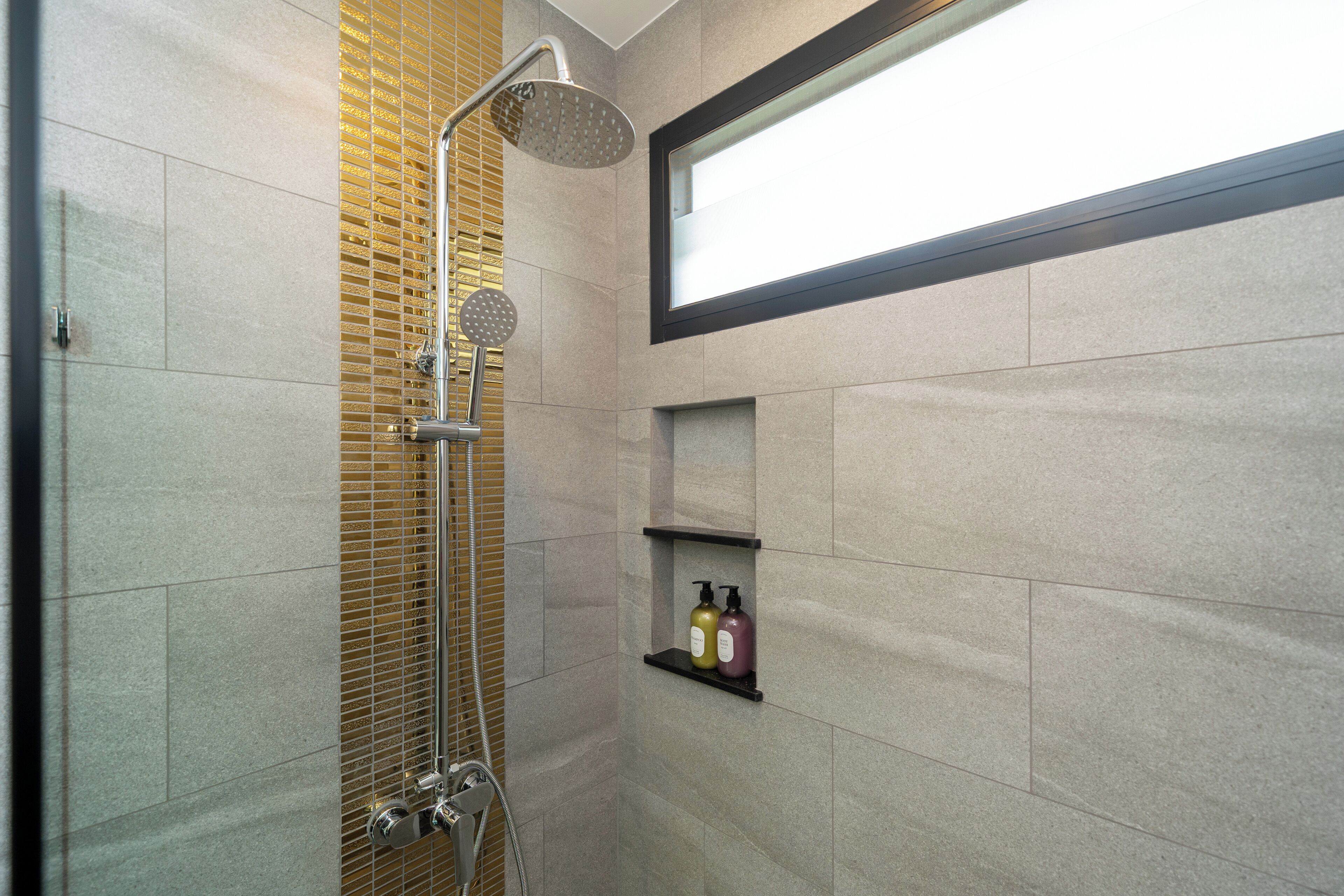 Een moderne badkamer met een douche, een raam en een plank met toiletartikelen.