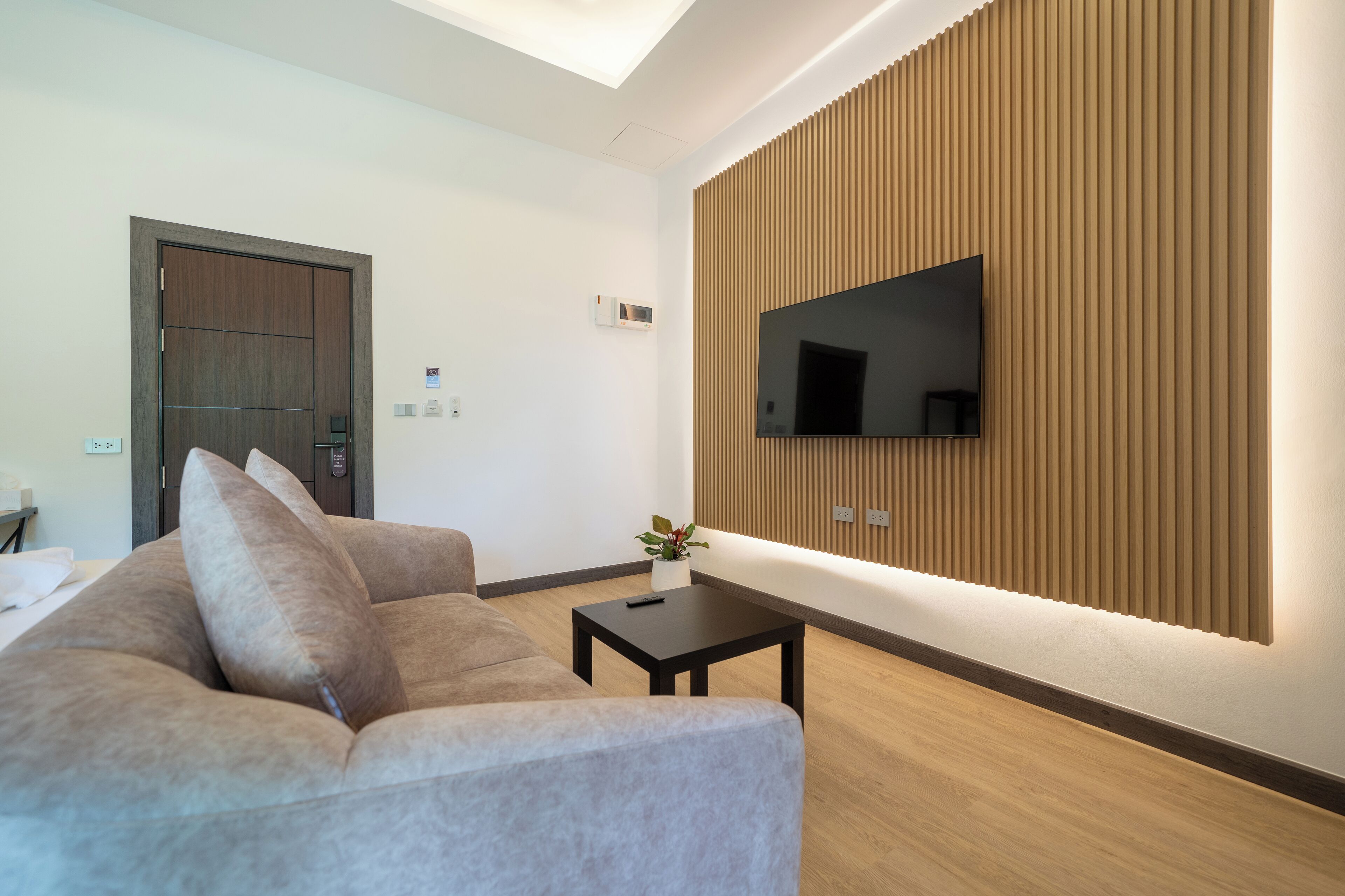 Ein modernes Wohnzimmer mit einer Couch, einem Couchtisch, einem an einer Holzvertäfelung befestigten Fernseher und einer Tür im Hintergrund.