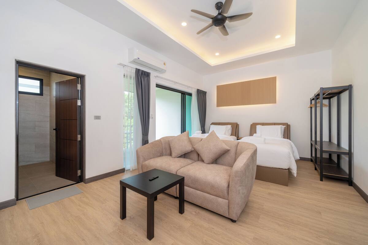 A modern hotel room with a sofa, two beds, a ceiling fan, and a built-in shelf.