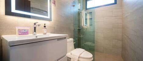 A modern bathroom with a white sink, toilet, and glass shower enclosure.