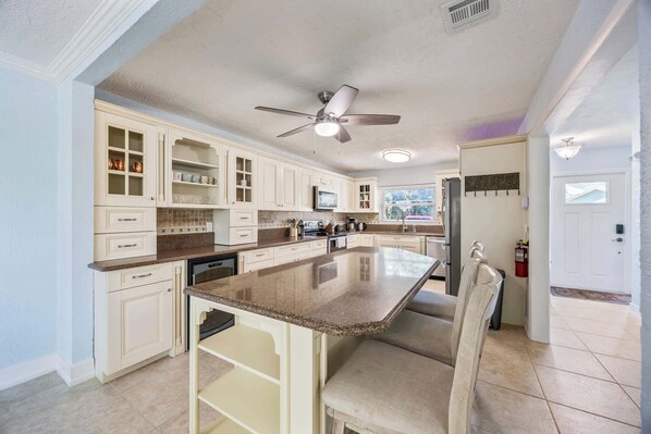 A spacious kitchen with white cabinetry, a large island, and a ceiling fan.