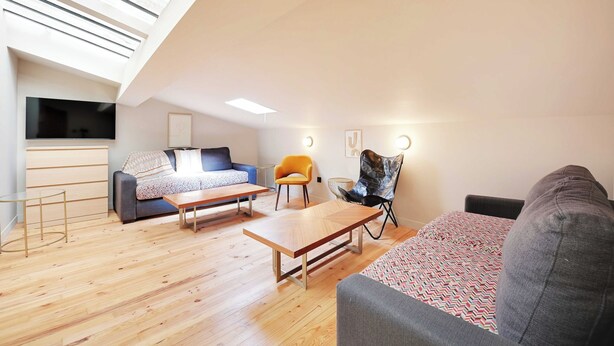 A modern living room with a sloped ceiling, wooden flooring, a sofa, a coffee table, a TV, and a chair. - Charming Apt - 2bd/10p - Buttes aux Cailles (Paris)