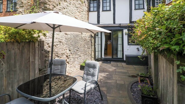 A courtyard with a stone wall, a wooden fence, a white umbrella, and a table with chairs.
