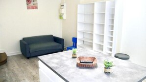 Een woonkamer met een grijze bank, een bijzettafel met een mand en potplanten, een witte boekenkast en een blauwe stoel.