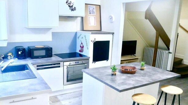 Een moderne keuken met witte kasten, een magnetron, een koffiezetapparaat en een klein eiland met krukken.