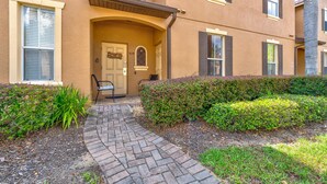 A building with a brick pathway leading to a door, a bench, and a well-maintained hedge.