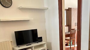 A living room with a flat-screen TV on a white entertainment unit, wooden flooring, and a door leading to a dining area. - Termini Apartment by Ghor (Rome)