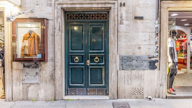Fachada de un edificio con una puerta verde, un maniquí en la entrada y un letrero con texto escrito a mano.
