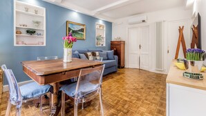 Un comedor con una mesa y sillas de madera, un sofá azul y un armario blanco con estantes frente a una pared azul.