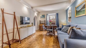 Una sala moderna con suelo de madera, un sofá azul, una mesa de comedor con sillas, un televisor y una escalera de madera.