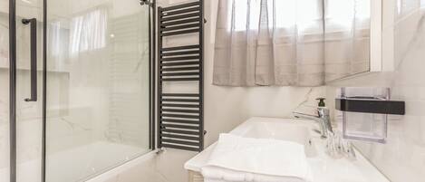 A modern bathroom with a glass-enclosed shower, a white sink with a mirror, and a towel rack.