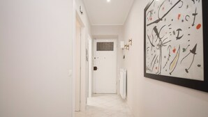 Een gang met een witte deur aan het einde, een radiator aan de muur en een lijst met abstracte kunst.