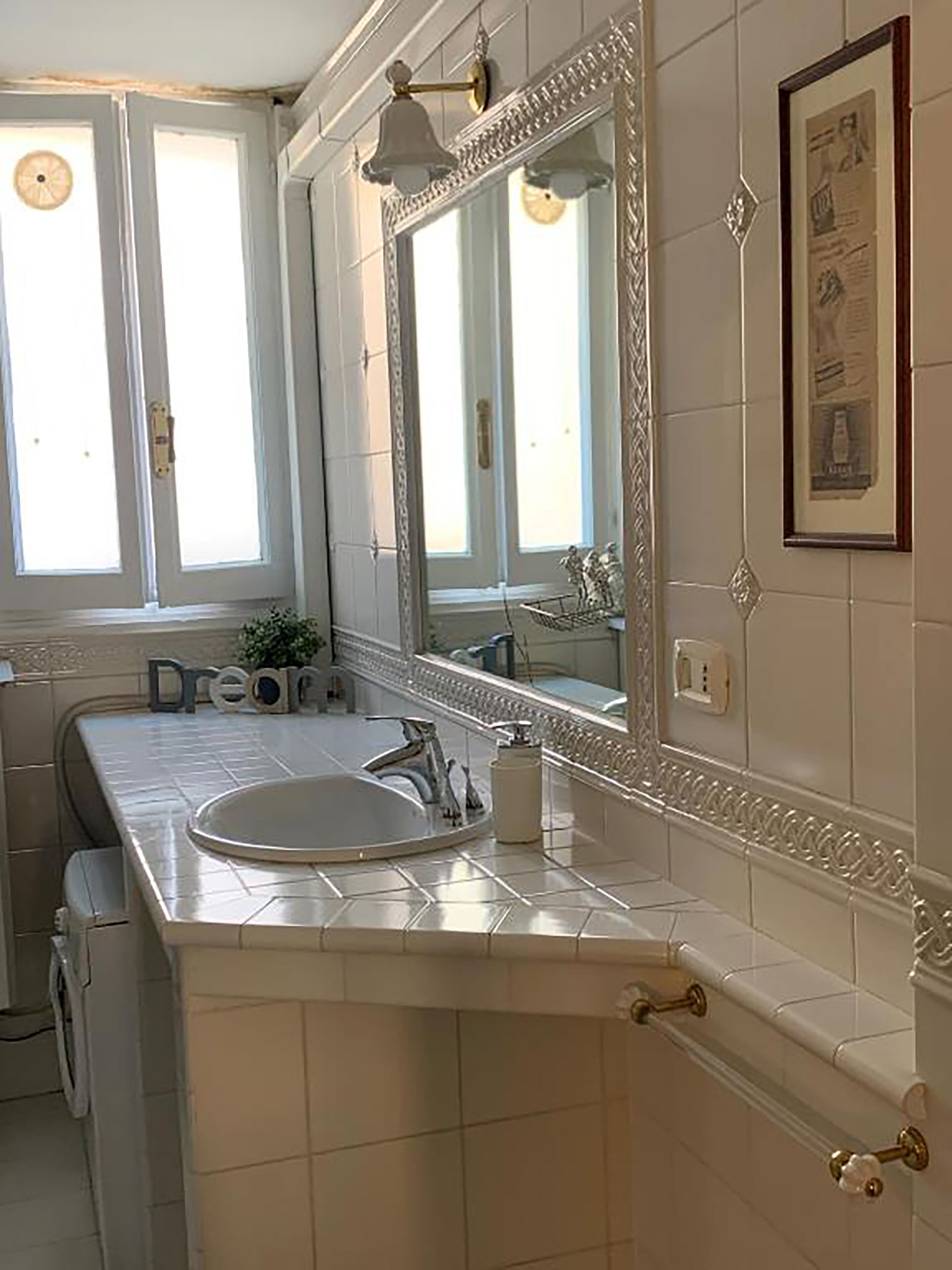 A bathroom with a large mirror, a sink, and a window.