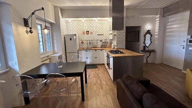 Een compacte keuken met een witte metselwerkachtergrond, een centraal eiland en een eethoek met een tafel en stoelen.