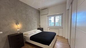Een slaapkamer met een bed, een nachtkastje, een wandlamp, een raam en een airconditioning.