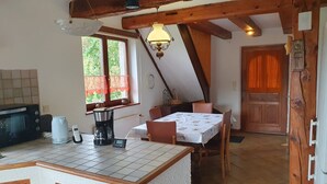A kitchen with a tiled countertop, a coffee maker, a kettle, and a microwave. There is a dining table with chairs and a window with curtains. - Charming Cottage with Vosges Mountain Views | Perfect for Walkers | Pets | WiFi  (Neuve-Église)