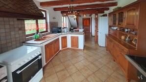 A kitchen with wooden cabinets, a white stove, and a tiled floor. - Charming Cottage with Vosges Mountain Views | Perfect for Walkers | Pets | WiFi  (Neuve-Église)