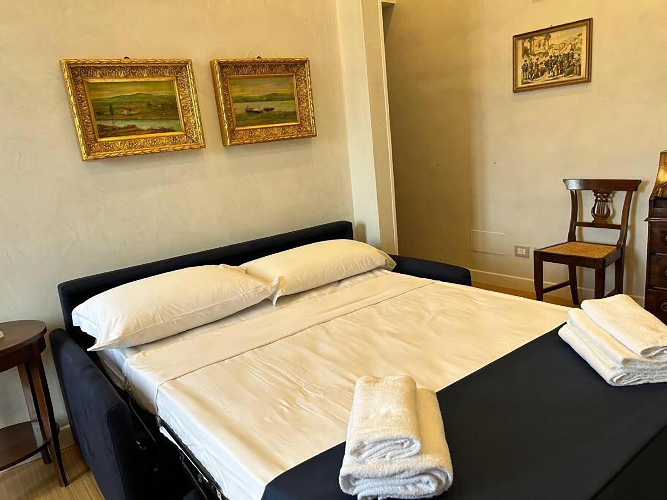 A neatly made bed with white linens and two paintings on the wall.
