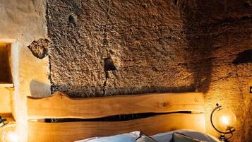 Une chambre confortable avec un mur en pierre rustique, une tête de lit en bois et un lit recouvert de draps blancs et agrémenté de plusieurs oreillers.
