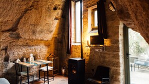 Une pièce mansardée chaleureuse, avec un mur en pierre rustique, une cheminée, une table à manger avec des chaises et une grande fenêtre laissant entrer la lumière naturelle.