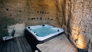 Un bain à remous dans une pièce aux murs de pierre, avec un banc en bois et une chaise.