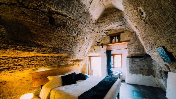 Une chambre avec un plafond en pierre, un lit avec une literie blanche et une table de chevet avec une lampe.