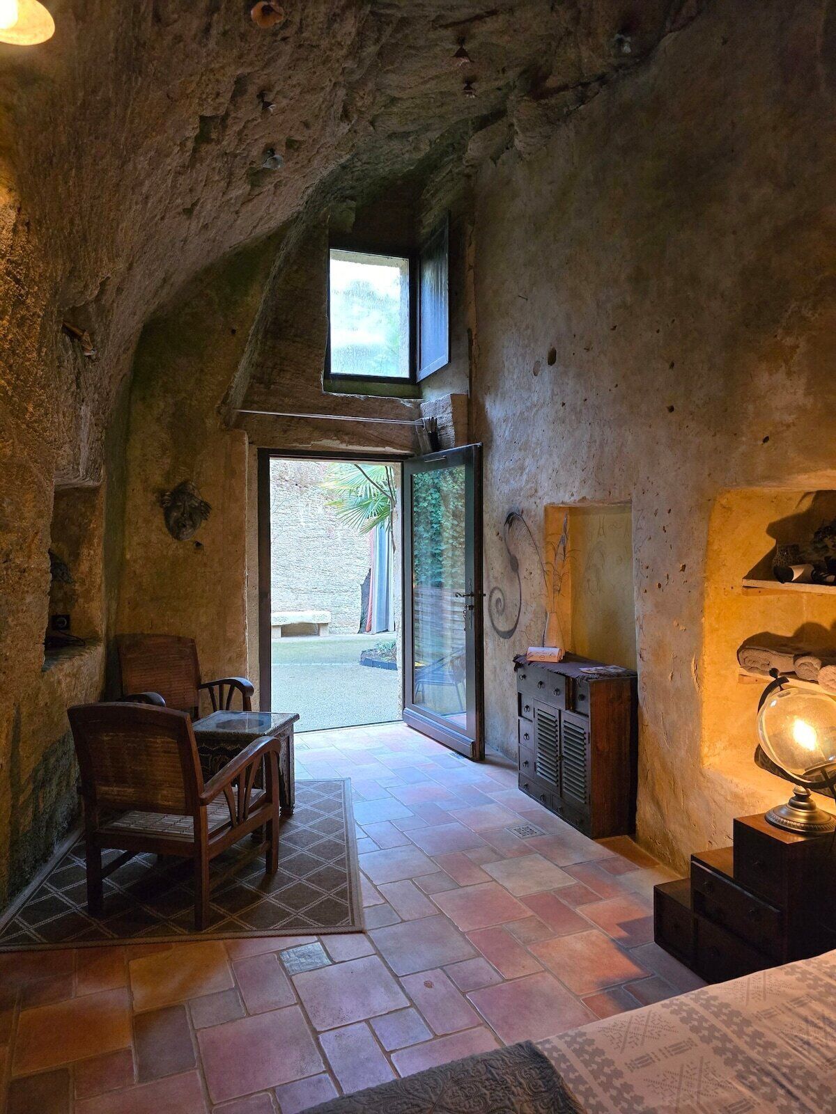 Un intérieur rustique avec un plafond en pierre, une table et des chaises en bois, une porte vitrée donnant sur l’extérieur et un globe terrestre posé sur un socle.