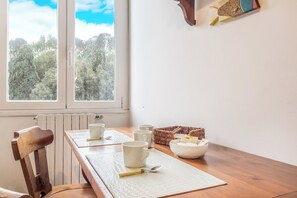 Ein Essbereich mit einem Holztisch, weißen Stühlen und Blick auf Bäume durch ein Fenster.