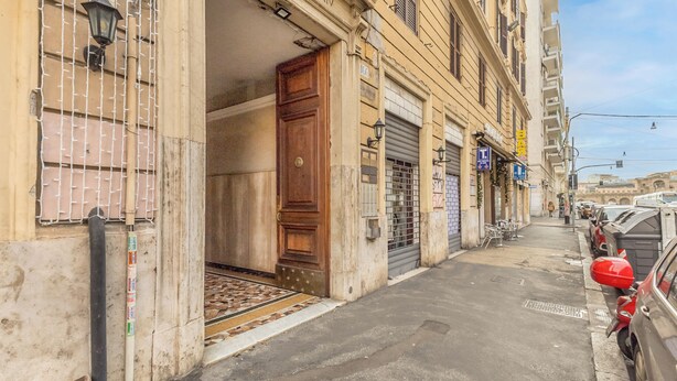 Una calle estrecha con coches estacionados, la entrada de un edificio con una puerta de madera y una reja de metal.