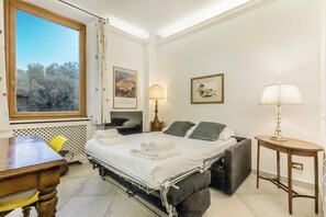 Ein Hotelzimmer mit Bett, Nachttisch, Lampe und einem Fenster mit Blick auf Bäume.