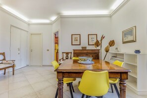 Un coin repas avec une table en bois, des chaises jaunes, des tableaux encadrés au mur et une porte blanche.