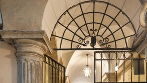 An arched doorway with a metal gate, a column, and a hallway leading to a room with a ceiling light.