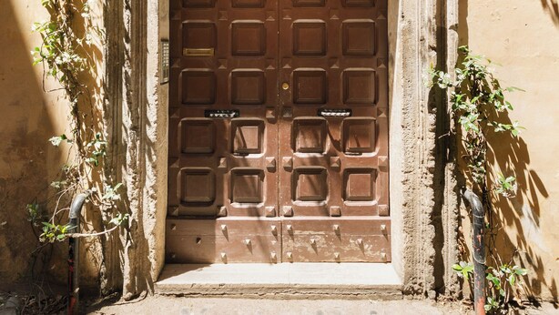 A brown wooden door with a decorative metal frame, set in a stone wall with a small window above.