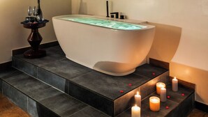 A modern bathroom with a freestanding bathtub, a small table with glasses and a bottle, and candles on the floor.