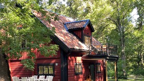 A red wooden cabin with a balcony, white chairs, and a gravel path. - Spectacular 6-bed house in beautiful manor park (Mariefred)