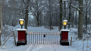 A snow-covered gate with two lanterns on either side, leading into a forested area. - Spectacular 6-bed house in beautiful manor park (Mariefred)