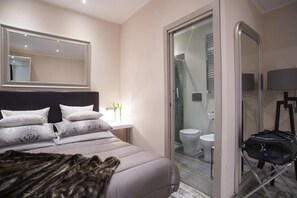 Un dormitorio moderno con una cama grande, un espejo junto a la cama y un baño con ducha e inodoro.