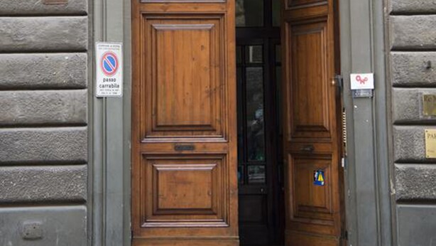 A wooden double door with a metal lattice design above it, set in a stone wall with numbered plaques.