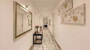 A hallway with a white floor, a mirror, and two framed artworks on the walls.