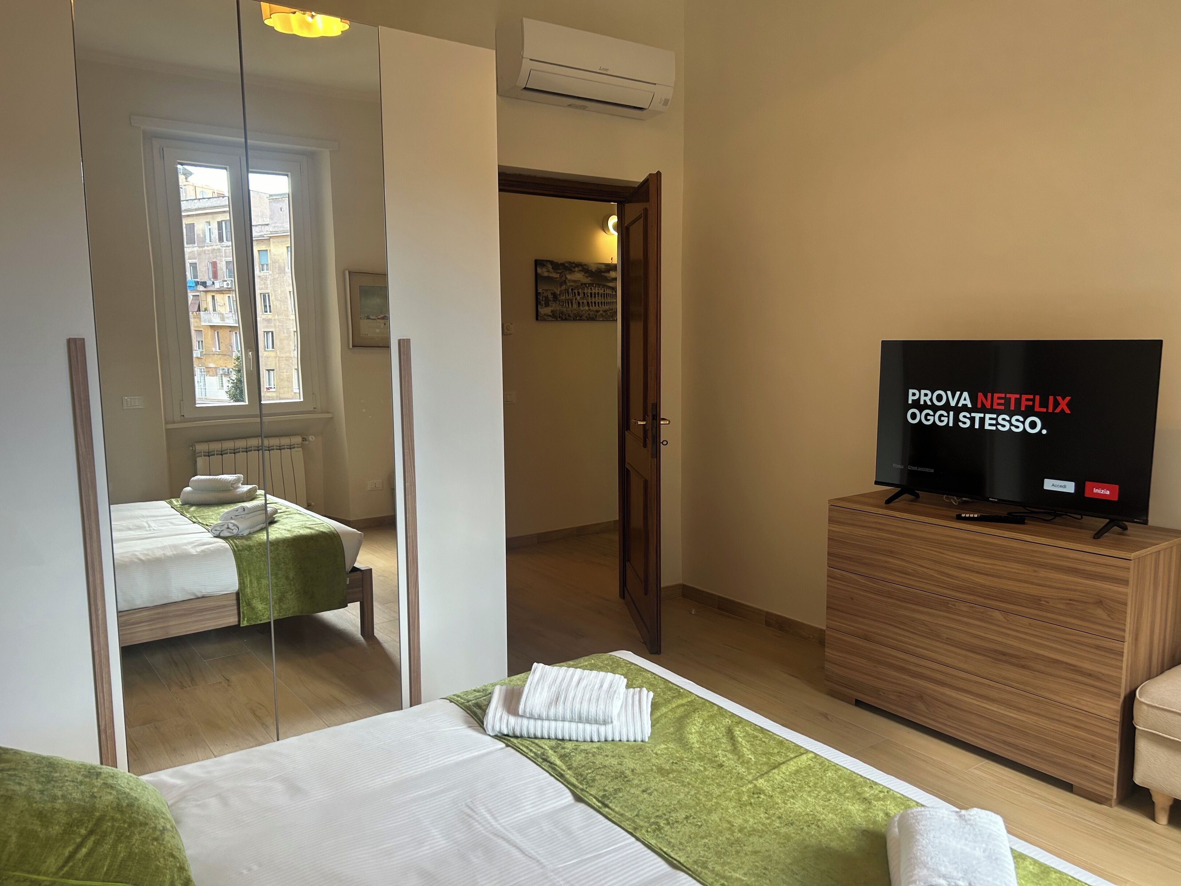 Hotellihuone, jossa on sänky, puinen lipasto ja sen päällä televisio sekä ikkuna, josta avautuu näkymä rakennuksiin.