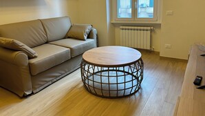 Un salon moderne avec un canapé beige, une table basse ronde en bois et une fenêtre donnant sur des immeubles.