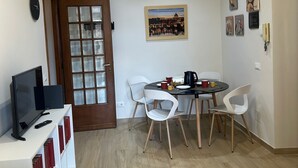 Un espace de vie compact comprenant un coin repas, un téléviseur et une porte dotée de panneaux en verre dépoli.