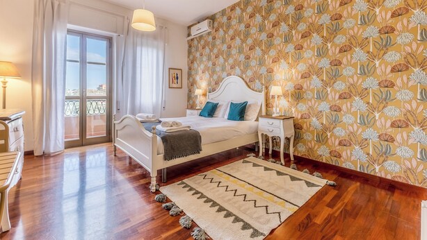 Une chambre à coucher avec un lit, des tables de chevet, une fenêtre avec des rideaux, un mur à motifs et un plancher en bois.