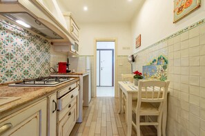 Una cocina estrecha con estufa a gas, una olla roja y salpicadero de azulejos.